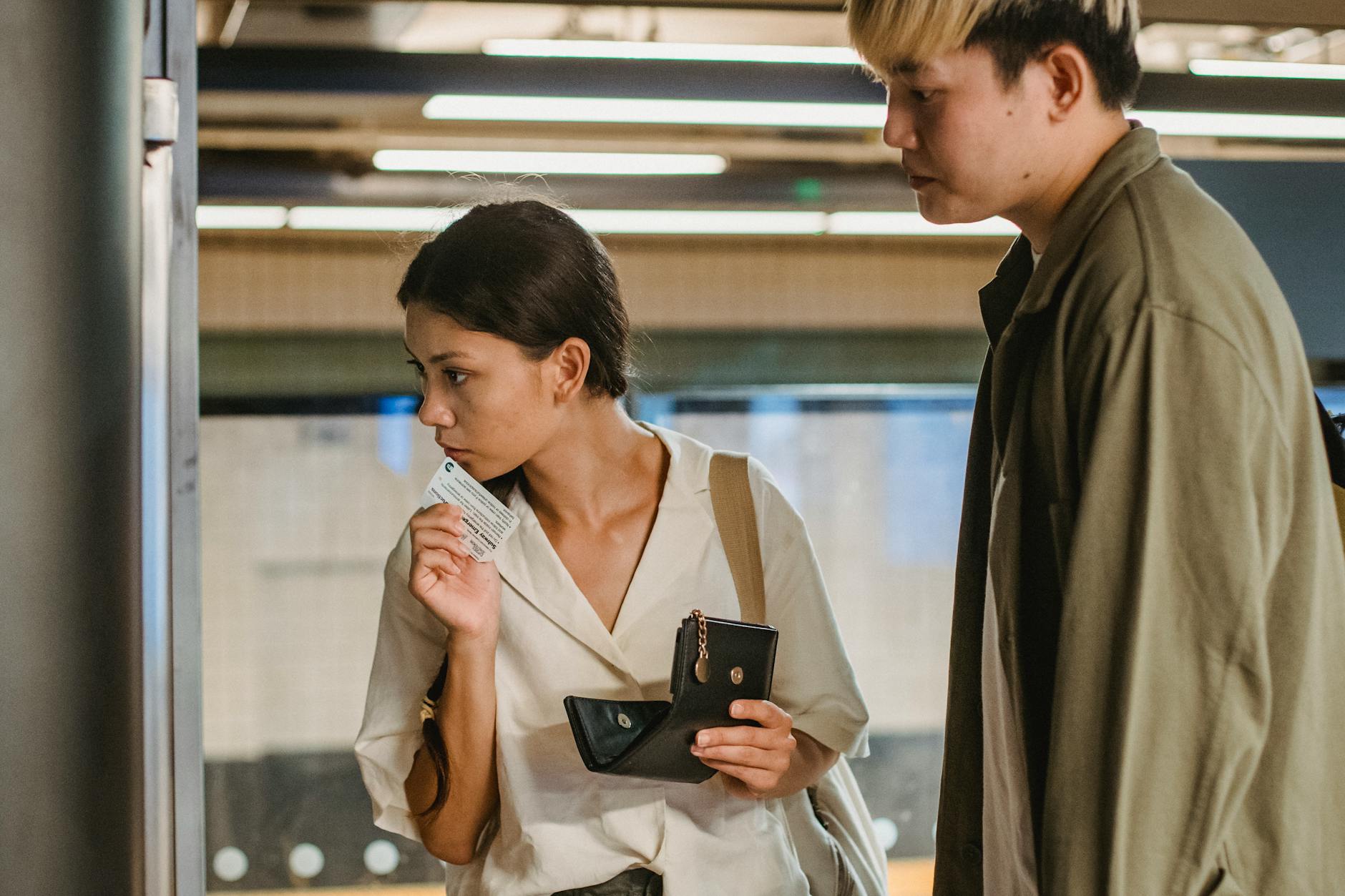 Konzentriertes Asiatisches Paar, Das Ticket Am Bahnhof Kauft